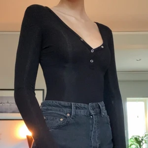 Svart body i superskönt material - Svart ribbad långärmad body med knappar. Knäppning nedtill. Köparen står för frakten. 