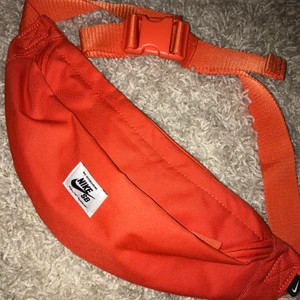 Nike Orange midjeväska - Så gott som ny orange midjeväska. Inte kommit till användning. Två fack ett mindre och ett stort. Justerbar . Både till killar och tjejer 