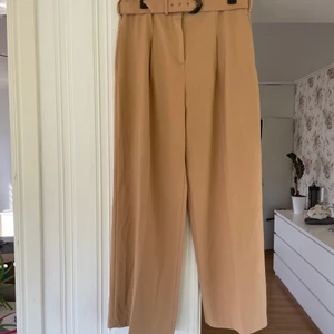 Lösa kostymbyxor  - Brunbeiga lösa kostymbyxor med bälte i midjan 