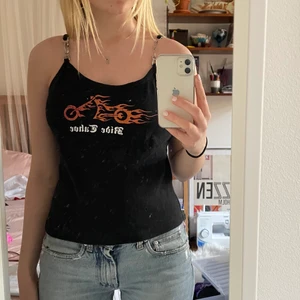 Coolt linne med motorcykel-tryck - Svart linne med en orange glittrig motorcykel och texten Ride Tahoe. Finns metall detaljer på banden, det ena är trasigt och lagat med säkerhetsnålar men märks inte så mycket. Det har extra tyg vid brösten så funkar bra utan bh. Köpare betalar frakten. 