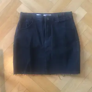 Svart jeanskjol i ganska elastisk denim. Trasad kant nedtill. Aldrig använd, etiketten sitter kvar. Storlek 38