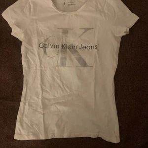 Vit Calvin Klein t-shirt silvrigt motiv - Säljer min helt oanvända CK tshirt med silvrigt och svart motiv på framsidan. Köpt för ca 1år sedan för 400kr, säljer antingen separat för 100kr eller tillsammans med de andra (se mina andra annonser) för 350kr (dvs 4 CK t-shirts för 350kr)