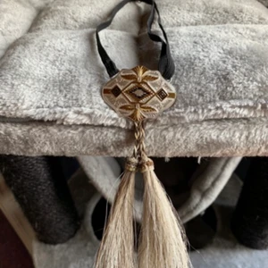 Bolo Tie, Southwest, Western Outfit. NY. - Bolo Tie från Montana Silversmiths USA. Bärs till skjorta under kragen. Montana silver och gulddetaljer. Ställbar resår i svart. Bredd: 5 cm, höjd: 3,8 cm. Tagel tofs längd: 8 cm. Äkta hästhår. Ny/Oanvänd. Frakt 📦 55 kr.