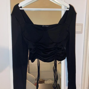Svart topp - Fin svart topp som man kan justera längden på med hjälp av snörena. Perfekt både till fest eller vardags. Den är i storlek M men skulle nog säga att den passar S också.