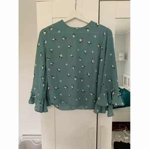 Blus  - Blus i fin grön färg med blommor, och med vida ärmar och volanger. Väldigt fin. Köpt för ca 2-3 år sen men endast använd ett fåtal gånger. Felfri. 