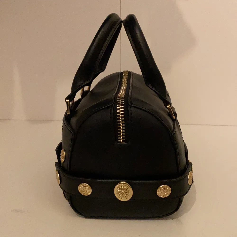 En mindre svart bowler väska med guld detaljer från Topshop. Det finns ett ytterfack, samt en korthållare i huvudfacket. Är i topp skick! B:14L:20H:14 (cm). Laukut & Käsilaukut.