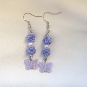 Söta fjärils örhängen  - Ett par fina örhängen med en fjäril som glänser jättefint! De lila pärlorna är handgjorda av mig. Örhängena är superfina att ge bort som present till någon eller till sig själv 💜 Är osäker på om krokarna är nickelfria. Frakt tillkommer på 13kr 