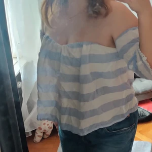 Off-Shoulder topp - Säljer vidare denna extremt fina off shoulder topp i vitt och blått!! Ärmarna är av elastisk resår i toppen och håller upp ärmarna vilken längd du vill. Runt bysten är det en vit topp (som döljs under det blå/vita tyget) som man enkelt kan ta av och på med hjälp av en dragkedja i bak. Köptes sommaren 2016 och har inte använts sedan dess. Perfekt för varma sommardagar antingen som vardagsplagg eller vid lite finare tillfällen❣️❣️skicka privat för flera bilder