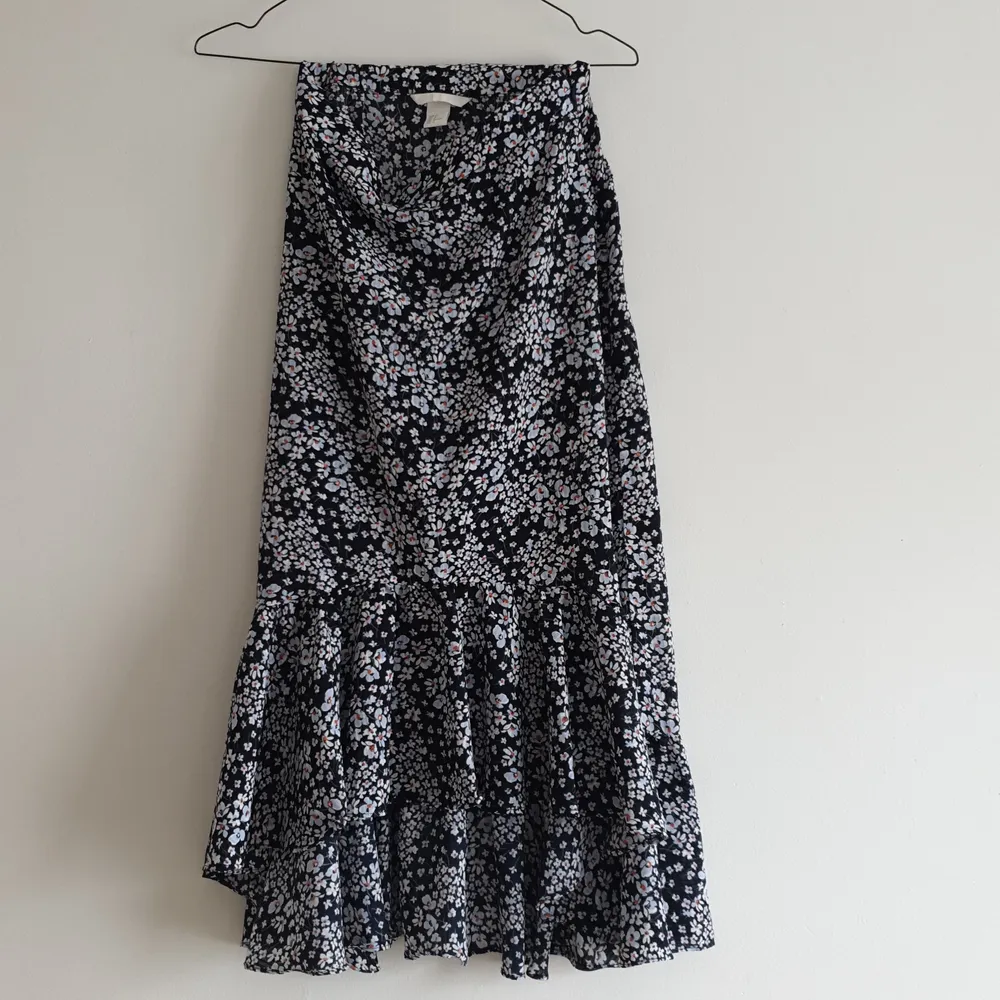 En blommig kjol med assymetrisk kant i volang. Från H&M, dragkedja i sidan. Färgen är en mörkare marinblå, nästan svart.. Kjolar.
