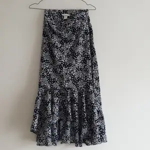 En blommig kjol med assymetrisk kant i volang. Från H&M, dragkedja i sidan. Färgen är en mörkare marinblå, nästan svart.
