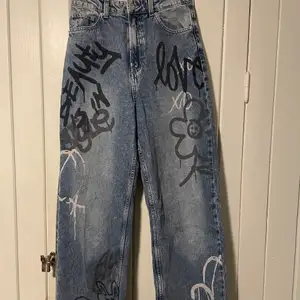 Ljusa vida jeans ifrån HM. Svart och vit graffiti text över stor del ut av byxorna. Köpta och använda en gång så är i nyskick💕