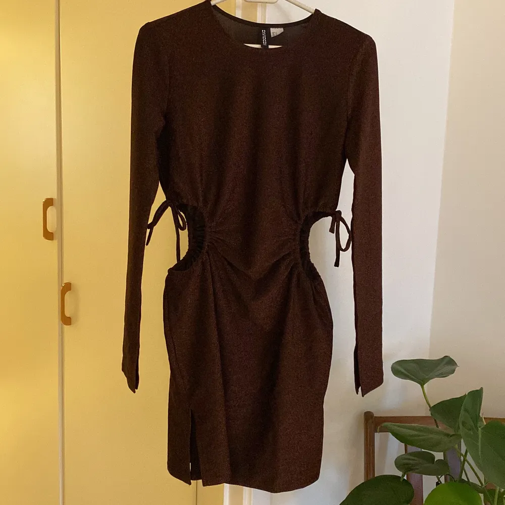 En kort brun glittrig klänning från H&M divided i strl S. Öppen i sidorna, går att justera hålen lite med knytningen. Kort öppen slits i sidan som visat på andra bilden. . Klänningar.
