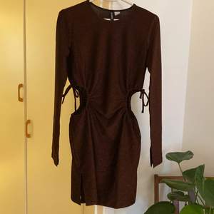 En kort brun glittrig klänning från H&M divided i strl S. Öppen i sidorna, går att justera hålen lite med knytningen. Kort öppen slits i sidan som visat på andra bilden. 