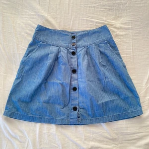 Blå jeans kjol  - En blå jeans kjol med svarta knappar. Har fickor på båda sidor. Köpt på secondhand men trots det är den i bra skick