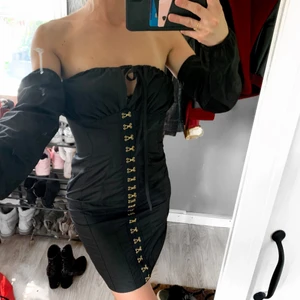 Svart klänning med lösa ärmar  - En svart klänning med gulddetaljer. Ärmar som man kan ha tillsammans med klänningen eller inte alls. Man kan även välja hur man vill knyta bandet vid bröstet. ClubL är märket. Storlek xs - inte jättestretchig. 