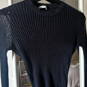 Svart ribbad tröja från Zara - Säljer en stilren svart ribbad tröja från Zara. Tröjan har en klassisk rund hals och långa ärmar, perfekt för lager-på-lager eller som den är. Passar både till jeans och kjol för en chic look.