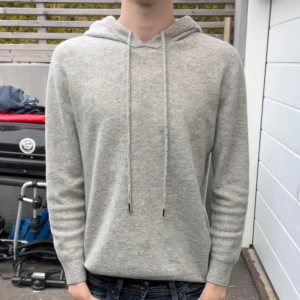 Grå Merinoull Hoodie - Säljer en stilren grå hoodie med långa ärmar och justerbar huva i merinoull. Perfekt för en avslappnad look.