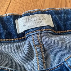 Blå jeans från Lindex - Säljer ett par klassiska blå jeans från Lindex. De har en rak passform och är tillverkade i denim med en knapp och dragkedja framtill. Perfekta för en avslappnad stil. I storlek 164