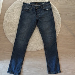 Mörkblå jeansbyxor - Snygga mörkblå jeansbyxor med klassisk femficksdesign och knappgylf. Perfekta för en avslappnad stil, dessa jeans har en rak passform som ger en tidlös look.