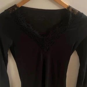 Svart spets tröja från Intimissimi - Säljer en elegant svart tröja från Intimissimi med vacker spetsdetalj vid halsringningen och ärmsluten. Tröjan är tillverkad i ett mjukt material med kashmir, vilket ger en lyxig känsla. Perfekt för en stilren look.