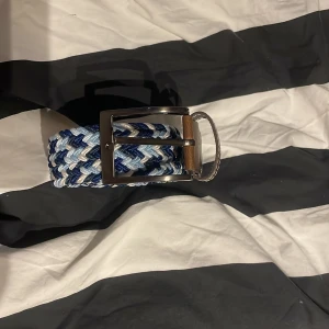 Flätat bälte i blå och vita nyanser - Snyggt flätat bälte i olika blå och vita nyanser med ett stilrent metallspänne. Perfekt för att ge en färgklick till din outfit. Köpt från Jeansbolaget för 200kr säljer mitt för 80kr!