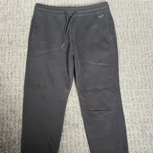 Svarta sköna mjukisbyxor från Hollister - Säljer ett par svarta mjukisbyxor från Hollister med snörning i midjan. Byxorna har en enkel design med en liten logga på sidan och är perfekta för en avslappnad stil.