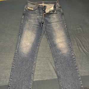 Blå jeans från Diesel - Snygga blå jeans från Diesel med klassisk femficksdesign och knappgylf. Jeansen har en lätt tvättad look och är perfekta för en avslappnad stil. Märkesdetaljer syns på fickan och insidan av linningen. W30 L 34