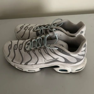 Nike TN  - Snygga Nike TN i vitt med gråa detaljer och mönster. Skorna har en unik design med synliga luftkuddar i sulan och snörning i vitt och blått. Perfekta för en sportig look. Pris kan diskuteras så tveka inte på att höra av er