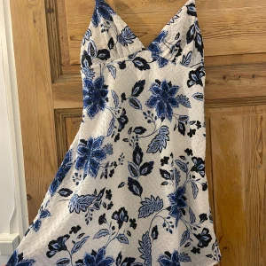 Blommig klänning - Charmig klänning med ett vackert blommönster i blått och svart på en vit bakgrund. Klänningen har smala axelband och en v-ringad design, perfekt för sommarens varma dagar. 🐳💙🩵🖤 Helt ny, lappen sitter kvar. 