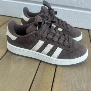 Adidas campus - bruna  - Använd enstaka gånger. Säljer då de är lite mer trånga för mig:( Perfekt kall brun nyans, kommer även med beige/vita snören som matchar detaljerna på skon. Även originalkartongen finns kvar. Enda defekten är att de blivit lite noppriga på insidan av hälen (se bild). Annars så gott som nya! Nypris: 1349 kr 