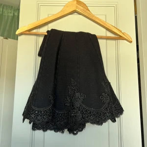 Svart kjol med spetsdetaljer från Wish by Anjee - En svart kjol med spetsdetaljer samt små pärlor. Ett robust material och högre midja med en utsvängning nedtill. En mindre medium.