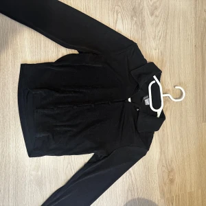 Svart långärmad kofta från H&M - Säljer en stilren svart kofta från H&M med långa ärmar och knappar framtill och lite skimmer. Perfekt för lager-på-lager och passar till många olika outfits. Ett måste i garderoben!