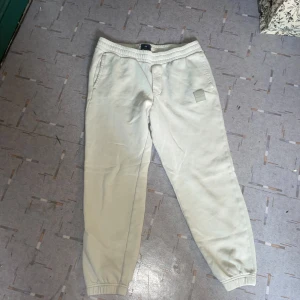 Beige mjukisbyxor från H&M - Säljer ett par bekväma beige mjukisbyxor från H&M i slim fit. Byxorna har elastisk midja och en stilren patchdetalj på sidan. En bakficka på höger baksida