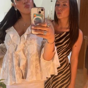 Vit blus med volanger - Säljer en elegant vit blus med volanger och v-ringning. Blusen har långa ärmar och ett vackert blommigt mönster. Perfekt för en stilfull look.