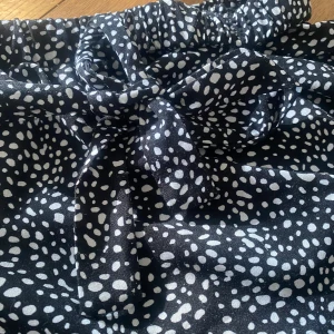 Svart och vit prickig kjol - Säljer en söt svart och vit prickig kjol med knytband i midjan. Kjolen har en volangdetalj som ger den extra charm. Den är i storlek 140 och är från Shein!!