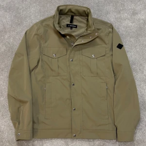 J.Lindeberg Bailey/Fieldjacket - Tja! Säljer nu denna riktigt schyssta gröna/beiga Fieldjackan från J.Lindeberg i nyskick! Modell Bailey. Jackan är somsagt i nyskick och har inga täcken på använding. size M. Skriv vid funderingar!