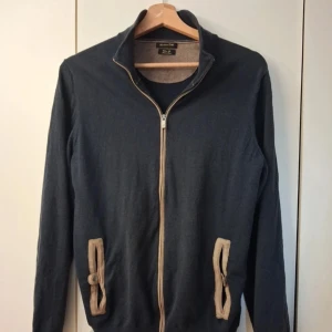 Blå cardigan tröja från Massimo Dutti - Tunn tröja med dragkedja från Massimo Dutti. Strl: M. Mycket fint skick. Den är i marinblåfärg med beige mockainlägg. Skriv vid intresse!