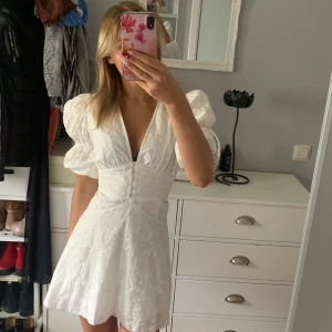 Vit kortklänning från Adoore - Superfin vit kortklänning från Adoore med puffärmar, v-ringning och markerad midja. Klänningen har broderade detaljer och knappar framtill. Perfekt för sommarens alla tillfällen och ger en romantisk vibe. Samt så finns det inga defekter, då den endast är använd 1 gång.🩷