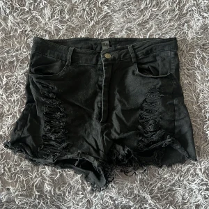 Svarta slitna jeansshorts från SHEIN - Svarta jeansshorts från SHEIN med hög midja och råa, fransiga kanter. Shortsen har slitna detaljer framtill och klassisk femficksdesign. Materialet är 97% bomull och 3% elastan vilket gör dem både bekväma och stretchiga. Perfekta för en edgy och avslappnad look.