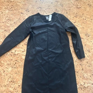 Svart långärmad klänning i syntet - En svart, långärmad klänning från H&M i glansigt syntetmaterial. Klänningen har en rak passform och rund halsringning, perfekt för dig som gillar en stilren look.