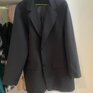 Svart kavaj från Boohoo, stl 40 - Stilren svart kavaj från Boohoo i klassisk modell med två knappar framtill och två fickor med lock. Kavajen har en rak passform och är helfodrad, perfekt för en snygg och enkel look. Materialet är mjukt och lätt, vilket gör den bekväm att bära.