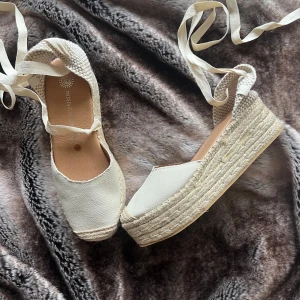 Beiga espadriller med platåsula - Snygga beiga espadriller från Musse & Cloud med platåsula i flätad jute och ovandel i canvas. Skorna har rund tå och knytband runt ankeln för en trendig look. Perfekta för varma dagar och ger en chill sommarvibe.