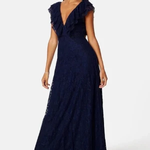 Marinblå långklänning med volang - Säljer en marinblå långklänning i spets med djup v-ringning och volangdetaljer längs axlar och urringning. Klänningen har öppen rygg och är ärmlös, vilket ger en elegant och trendig look. Perfekt för dig som vill sticka ut med en klassisk men modern stil. Passar om man ska på bröllop eller andra festligheter!