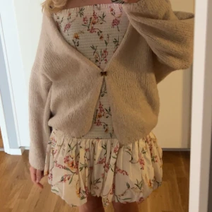 Blommig kortklänning med volang - Supersöt kortklänning med blommigt mönster i rosa och grönt på ljus botten. Klänningen är ärmlös och har smock upptill samt volangig kjol. Perfekt för sommarens alla tillfällen! Pris kan diskuteras 