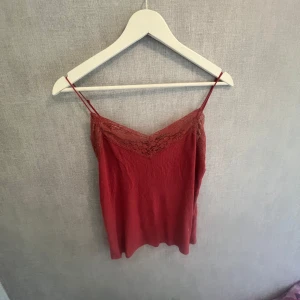 Röd linnetopp med spetsdetalj - Säljer en röd linnetopp från C i storlek S. Toppen har tunna axelband och v-ringning med snygga spetsdetaljer upptill. Materialet känns lätt och luftigt, perfekt för varma dagar eller lager på lager. Enkel men ändå elegant stil som lyfter vilken outfit som helst.