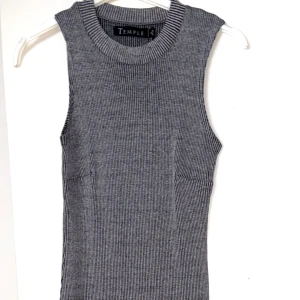 Grå ribbad ärmlös klänning från Temple - Säljer en grå, ribbad ärmlös klänning från  Temple. Toppen har en rund halsringning och smal passform. Perfekt att styla med jeans eller kjol för en clean look. Tunt, stretchigt material som sitter snyggt på kroppen.