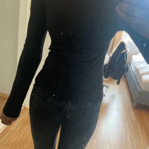 Svart långärmad tight tröja - En svart långärmad tröja med tight passform. Enkel och stilren design utan synliga detaljer eller mönster. Perfekt att matcha med jeans eller kjol för en clean look. Materialet känns mjukt och stretchigt, vilket gör den bekväm att bära hela dagen.
