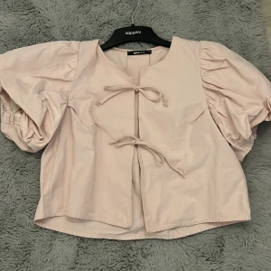 Ljusrosa blus med puffärm Gina Tricot - Supersöt ljusrosa blus från Gina Tricot med stora puffärmar och två knytband framtill. Blusen har en rak passform och är tillverkad i ett mjukt tyg som känns skönt mot huden. Perfekt för dig som vill ha en trendig och feminin look.