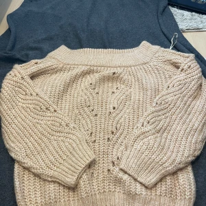 Beige stickad tröja från NA-KD - Supermysig beige stickad tröja från NA-KD i storlek S. Tröjan har ett chunky stickat mönster med snygga detaljer på ärmarna och framtill. Den har ribbade muddar och en rund halsringning. Perfekt för lager-på-lager under kyliga dagar.