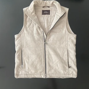 Väst från Oscar Jacobson - Stilren beige väst från Oscar Jacobson. Västen har tvåvägsdragkedja framtill och praktiska fickor med dragkedja. Perfekt att slänga över en hoodie eller skjorta för en clean look. Inga defekter. Skriv mod funderingar ✅ Pris kan diskuteras, skriv gärna vid funderingar 👍Nypris 3000
